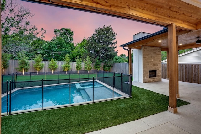 view of pool featuring a hot tub, an outdoor stone fireplace, a fenced backyard, a patio, and a yard