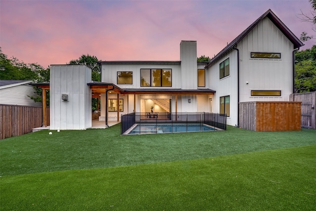 back of property at dusk with a yard, a fenced in pool, and a fenced backyard