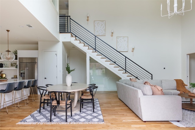living area with a high ceiling, stairs, light wood-style flooring, and a notable chandelier