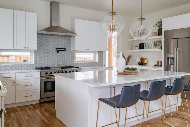 kitchen with high end appliances, tasteful backsplash, a center island, light stone counters, and wall chimney exhaust hood