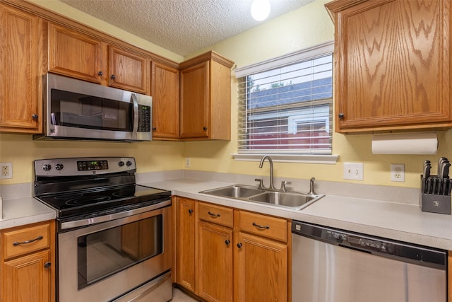 kitchen with a sink, a textured ceiling, appliances with stainless steel finishes, and light countertops