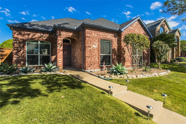 view of front facade with brick siding, a shingled roof, and a front yard