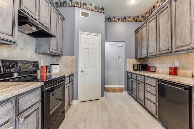 kitchen featuring visible vents, black electric range oven, baseboards, light wood finished floors, and under cabinet range hood