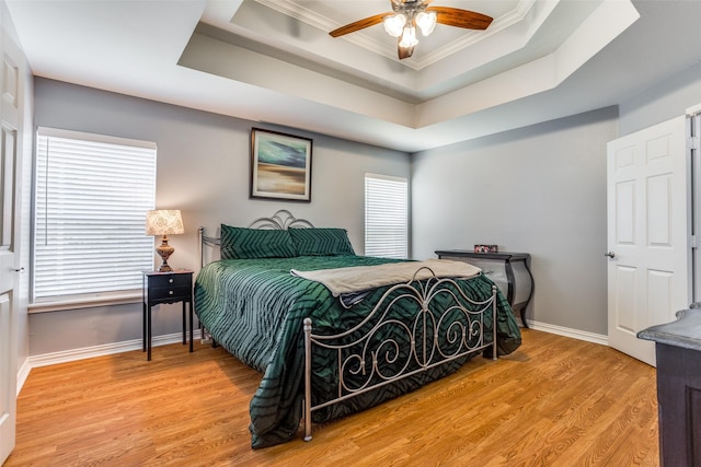 bedroom featuring ornamental molding, a tray ceiling, wood finished floors, and multiple windows