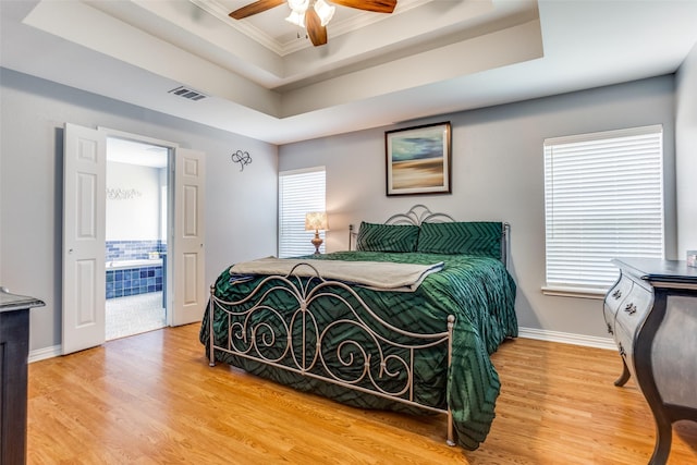 bedroom with visible vents, crown molding, a raised ceiling, baseboards, and light wood finished floors