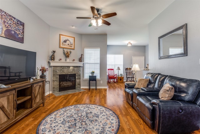 living area with baseboards, a ceiling fan, a fireplace with flush hearth, and wood finished floors