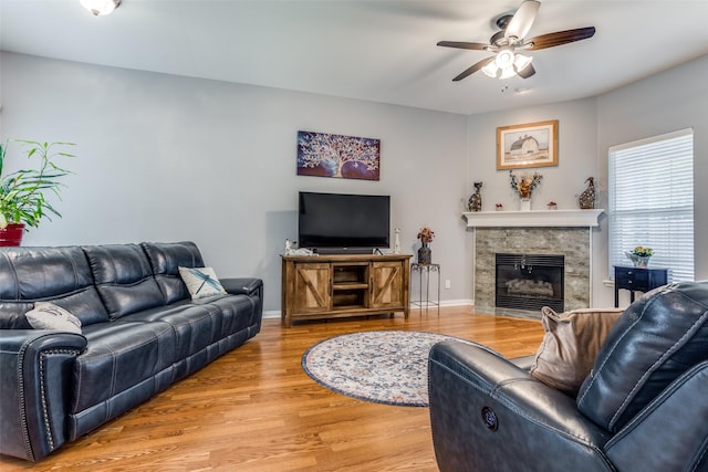 living area with light wood-type flooring, baseboards, ceiling fan, and a tiled fireplace