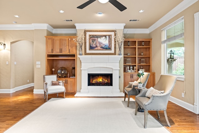 living area featuring ceiling fan, crown molding, wood finished floors, a lit fireplace, and baseboards