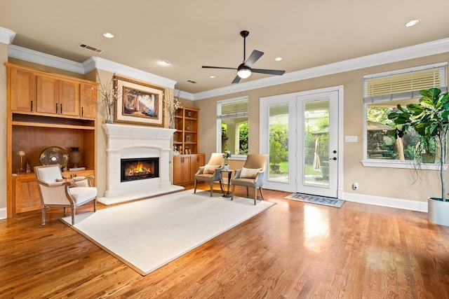 living area with ornamental molding, a lit fireplace, a ceiling fan, wood finished floors, and baseboards
