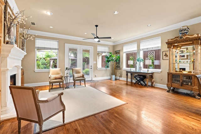 living area featuring crown molding, a ceiling fan, healthy amount of natural light, a warm lit fireplace, and wood finished floors