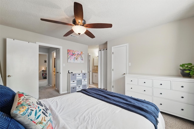 bedroom with a ceiling fan, a textured ceiling, light colored carpet, visible vents, and ensuite bathroom