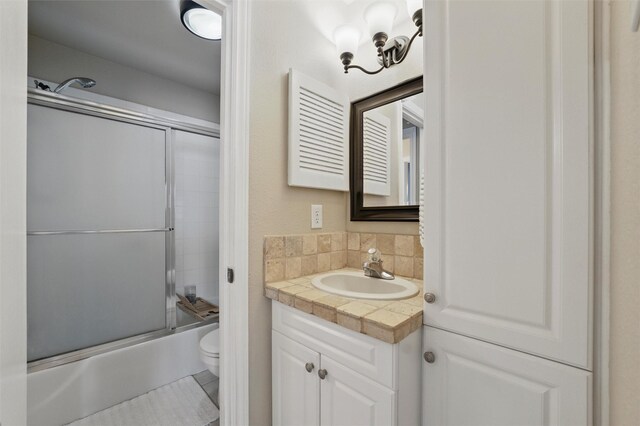 bathroom featuring vanity, tasteful backsplash, combined bath / shower with glass door, and toilet
