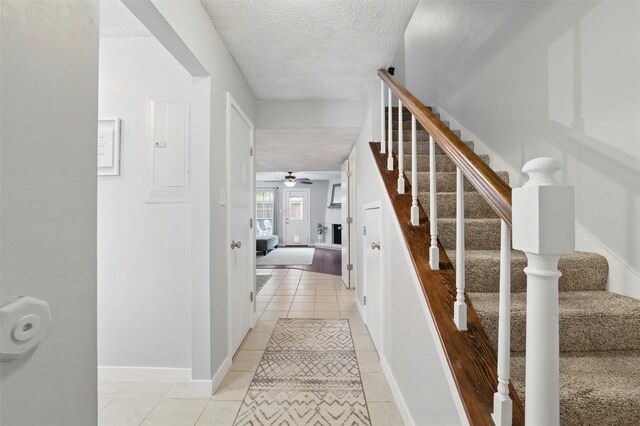 stairway with tile patterned flooring, a textured ceiling, ceiling fan, and baseboards