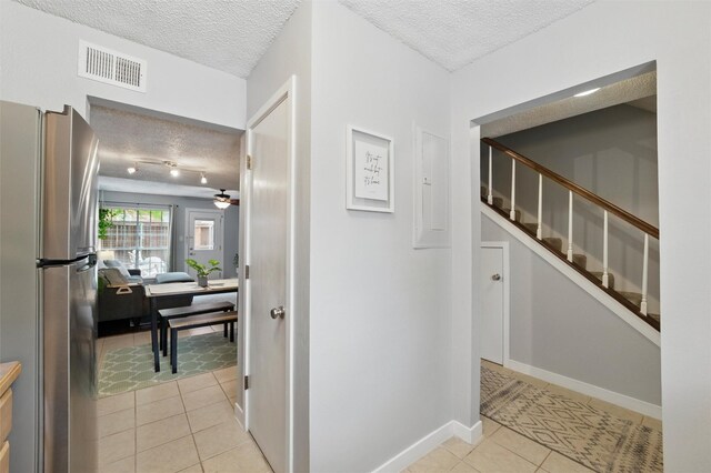 hall with a textured ceiling, baseboards, light tile patterned floors, visible vents, and stairway