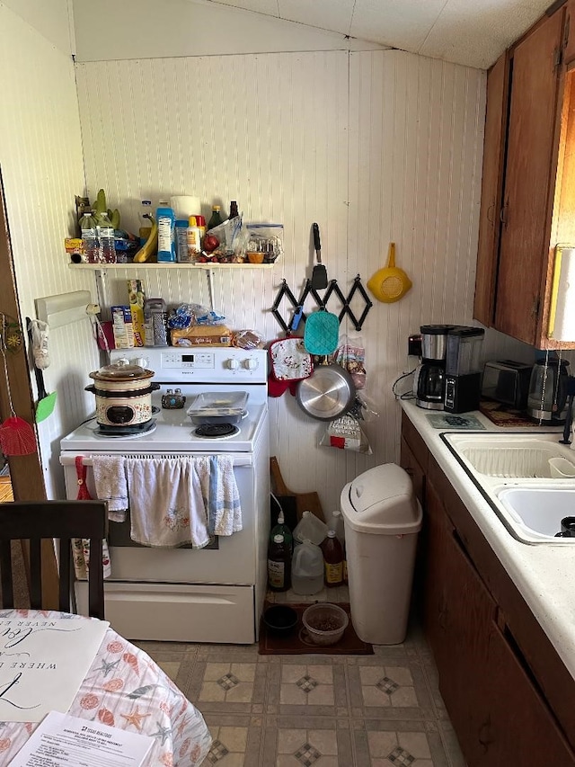 kitchen with a sink, white electric stove, wood walls, and light countertops