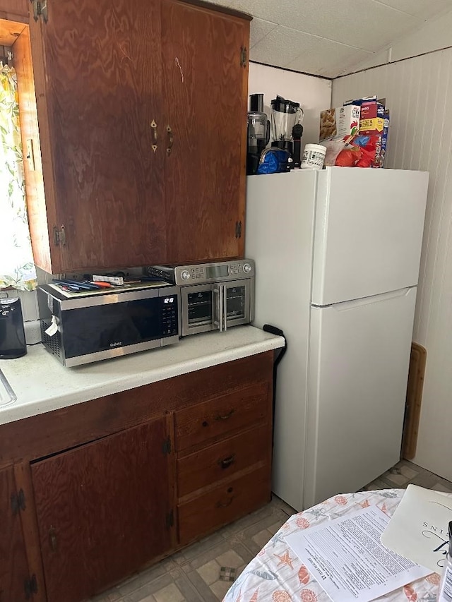 kitchen with freestanding refrigerator, stainless steel microwave, light floors, and light countertops