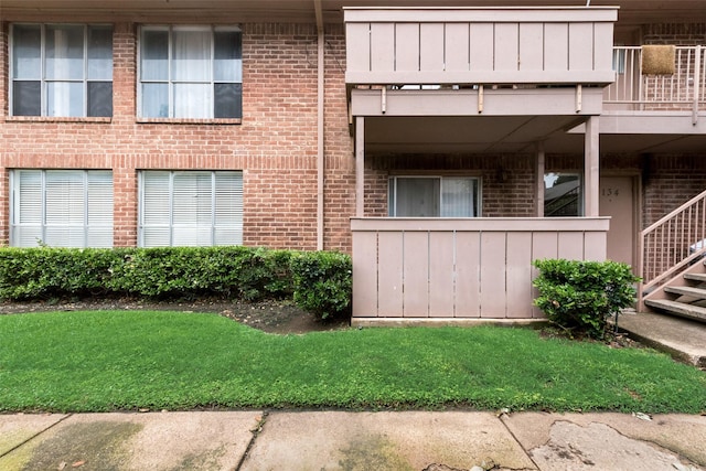 exterior space featuring a balcony, brick siding, and a lawn