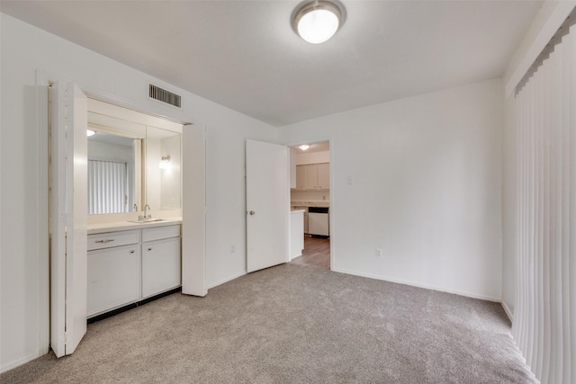unfurnished bedroom featuring light colored carpet, visible vents, a sink, baseboards, and connected bathroom