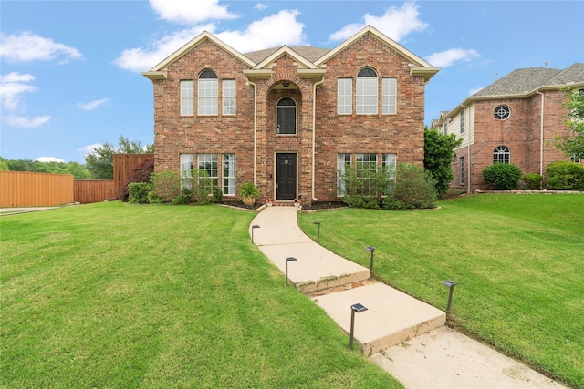 traditional-style home featuring brick siding, a front lawn, and fence