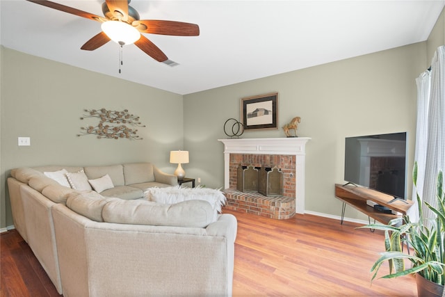 living room featuring baseboards, a brick fireplace, ceiling fan, and wood finished floors