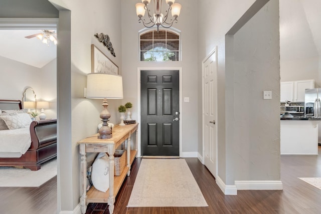 entryway with dark wood-type flooring, baseboards, ceiling fan with notable chandelier, and a high ceiling
