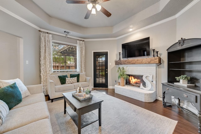 living room featuring a ceiling fan, a tray ceiling, visible vents, wood finished floors, and a fireplace