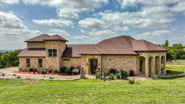 view of front of property with roof with shingles, stone siding, brick siding, and a front yard