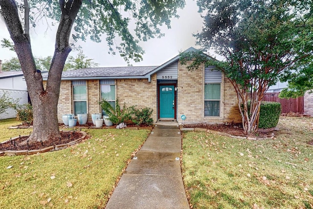ranch-style home with fence, a front yard, roof with shingles, and brick siding