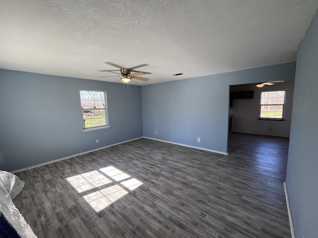 empty room with a textured ceiling, baseboards, dark wood finished floors, ceiling fan, and visible vents