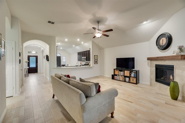 living area with ceiling fan, visible vents, arched walkways, lofted ceiling, and light wood-style floors