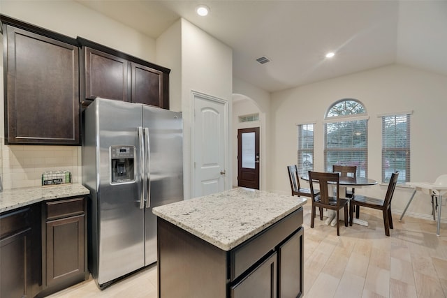 kitchen featuring visible vents, dark brown cabinetry, stainless steel refrigerator with ice dispenser, arched walkways, and backsplash