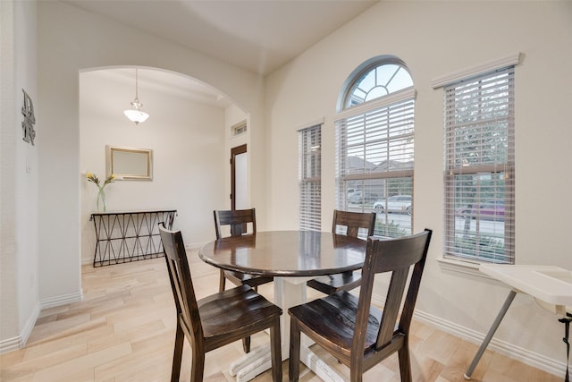 dining area with light wood-type flooring, arched walkways, and baseboards