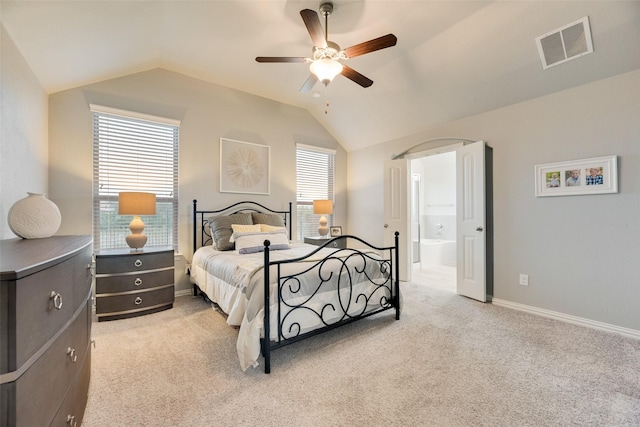 bedroom with a ceiling fan, light colored carpet, visible vents, vaulted ceiling, and ensuite bathroom