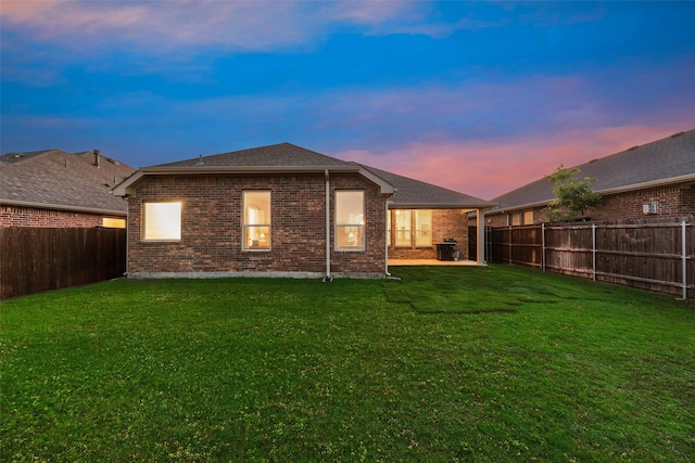back of house at dusk featuring a lawn, a fenced backyard, and brick siding