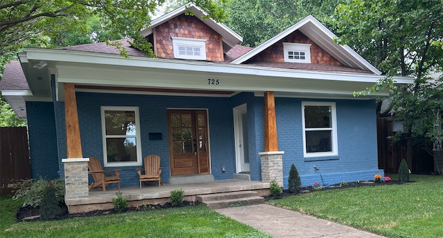 view of front of house with fence, a porch, a front lawn, and brick siding