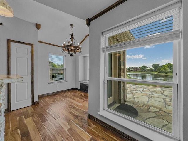 unfurnished dining area featuring baseboards, dark wood-style floors, a chandelier, a water view, and ornamental molding