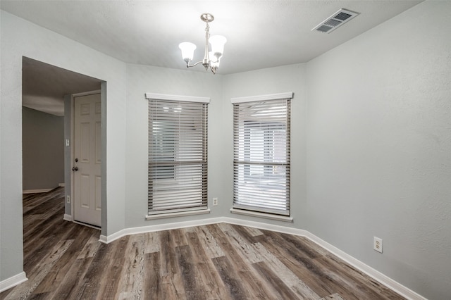 unfurnished dining area with baseboards, dark wood-style flooring, a chandelier, and visible vents