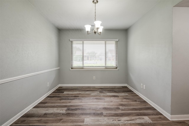 unfurnished room featuring baseboards, wood finished floors, and a chandelier