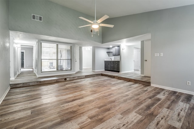 unfurnished living room featuring ceiling fan, visible vents, wood finished floors, high vaulted ceiling, and baseboards