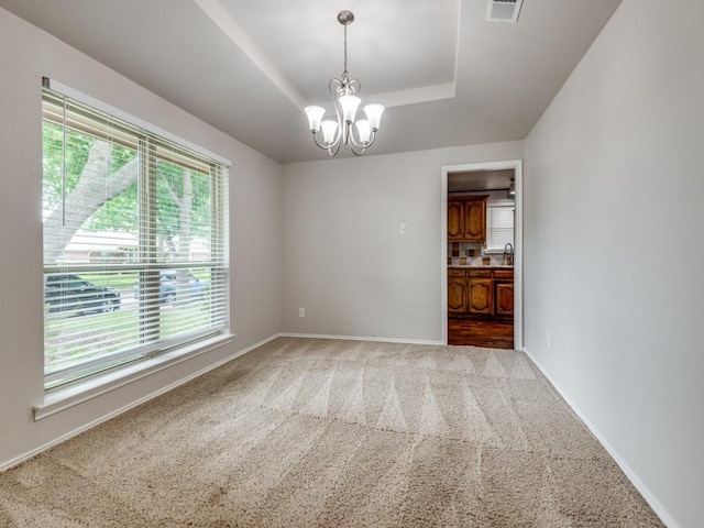 empty room with visible vents, baseboards, a tray ceiling, a chandelier, and carpet