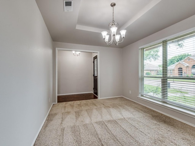 carpeted spare room with visible vents, a raised ceiling, baseboards, and a chandelier