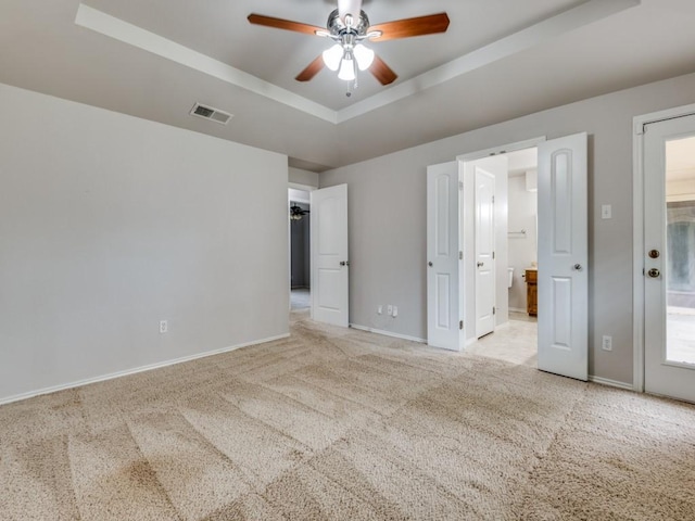 unfurnished bedroom with ensuite bath, visible vents, baseboards, a tray ceiling, and carpet flooring