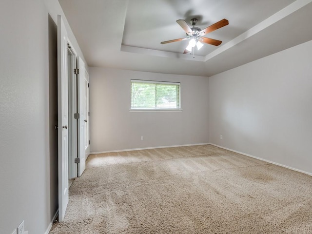 carpeted empty room featuring a raised ceiling, ceiling fan, and baseboards