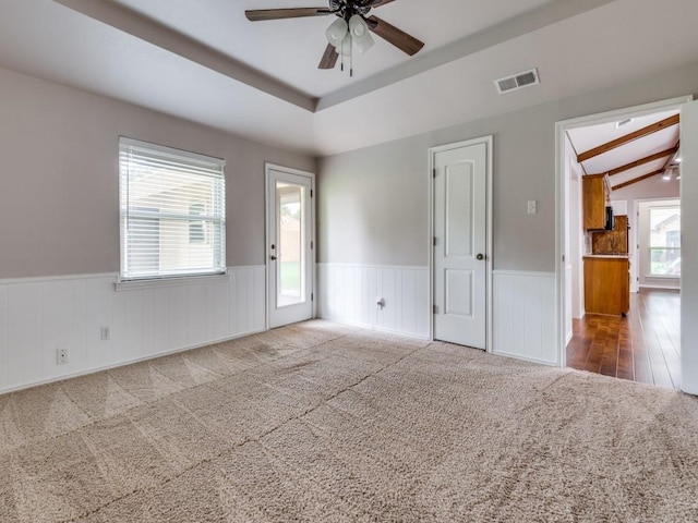 spare room featuring ceiling fan, visible vents, wainscoting, vaulted ceiling with beams, and carpet