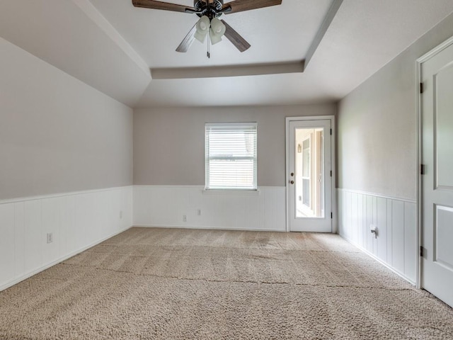 carpeted empty room with a tray ceiling, a ceiling fan, and wainscoting