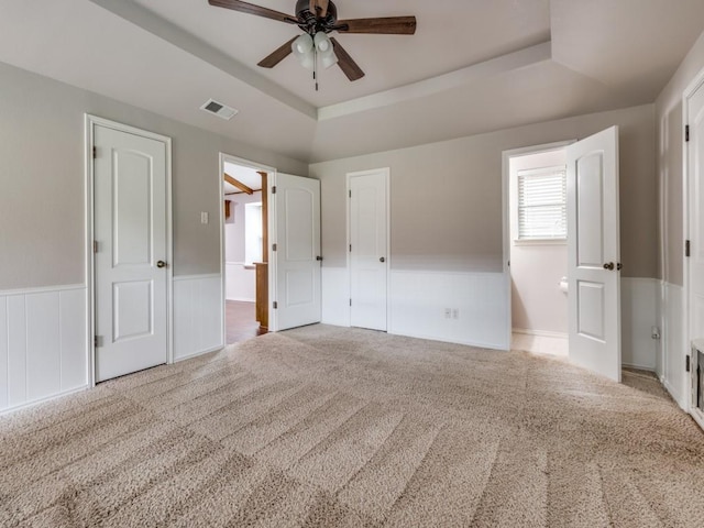 unfurnished bedroom featuring carpet floors, a wainscoted wall, a tray ceiling, and visible vents