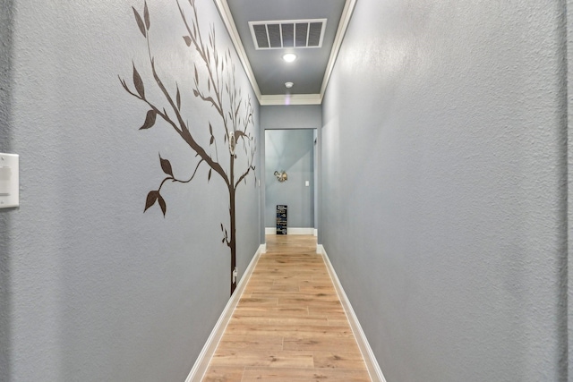 corridor with baseboards, ornamental molding, light wood finished floors, and visible vents