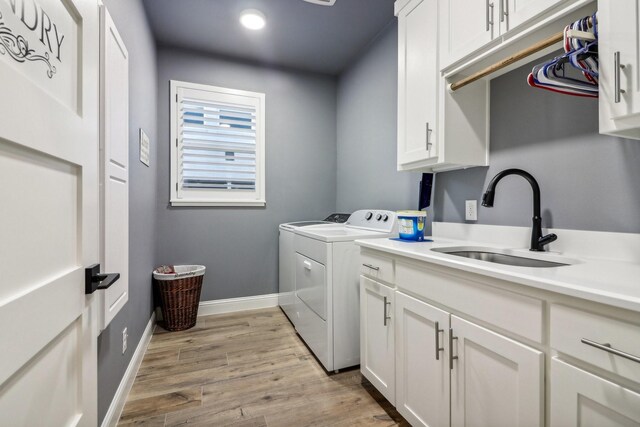 laundry area with washing machine and clothes dryer, cabinet space, a sink, baseboards, and light wood-style flooring