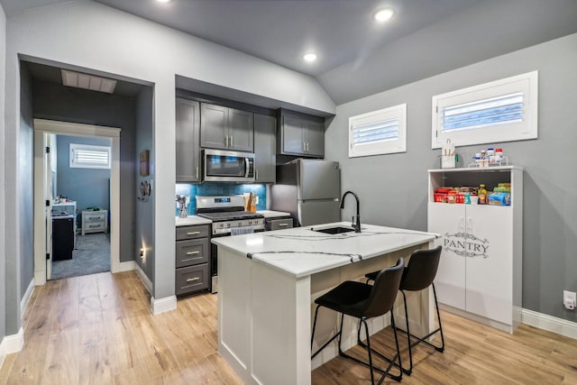 kitchen featuring light stone countertops, a sink, light wood finished floors, a breakfast bar, and stainless steel appliances