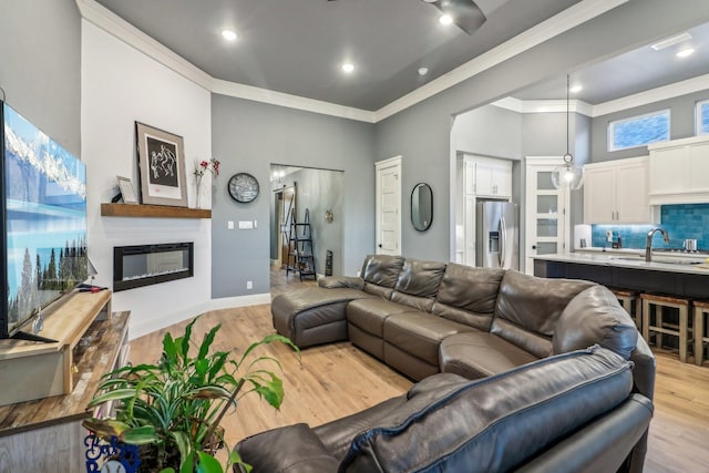 living room with crown molding, a glass covered fireplace, baseboards, recessed lighting, and light wood-style flooring